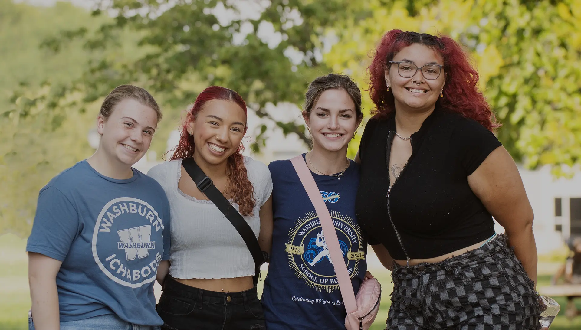 Four students smiling at camera on campus with trees in background