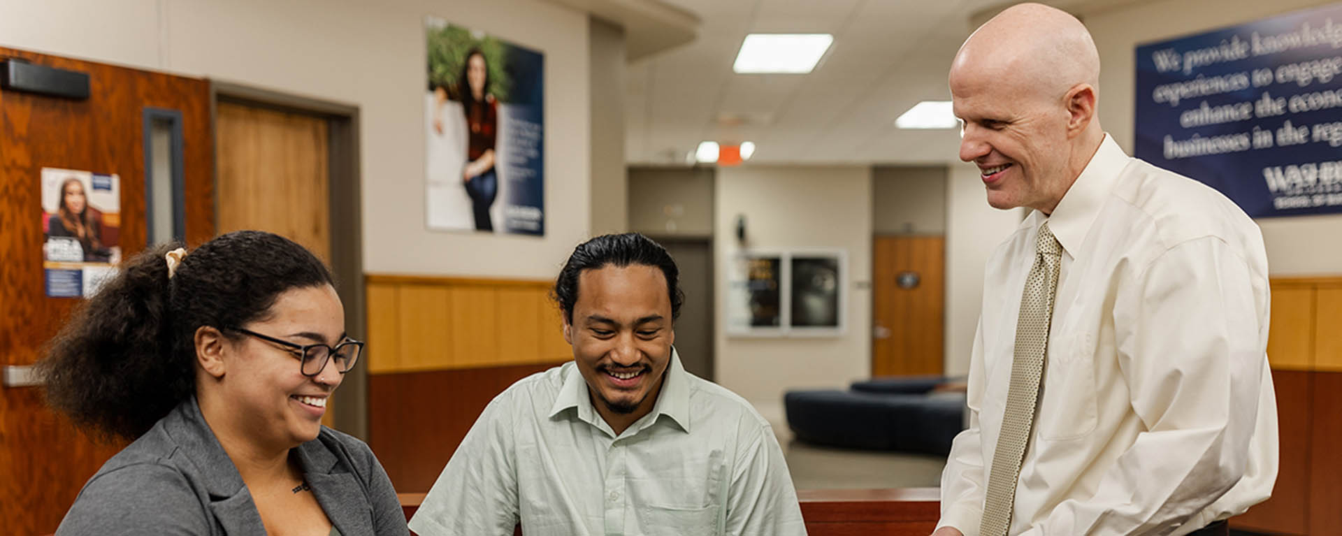 professor and students smiling and talking in lobby area of Henderson Hall