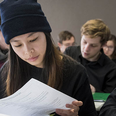 student in class reading paper at desk