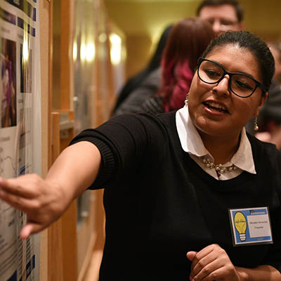 A student points to her Apeiron poster while talking.