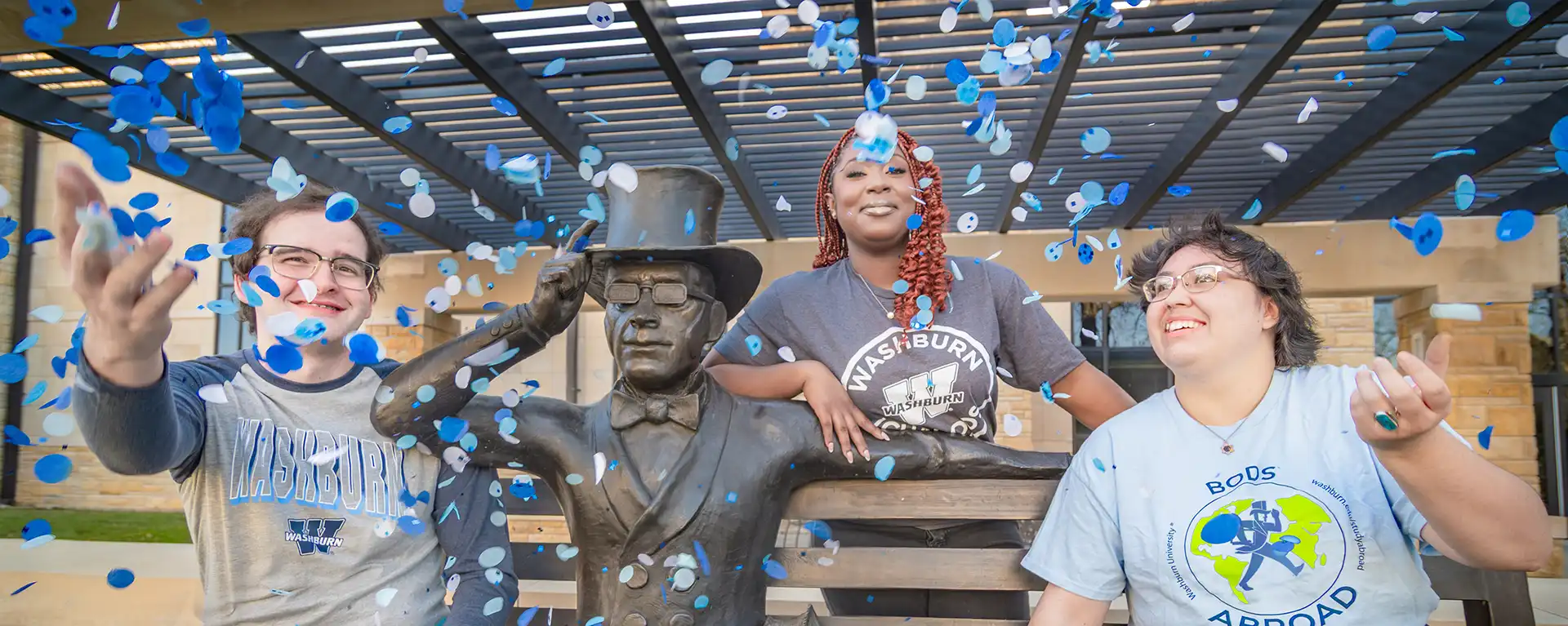 A group of students smile and pose for the camera while sitting next to the ichabod statue with confetti.