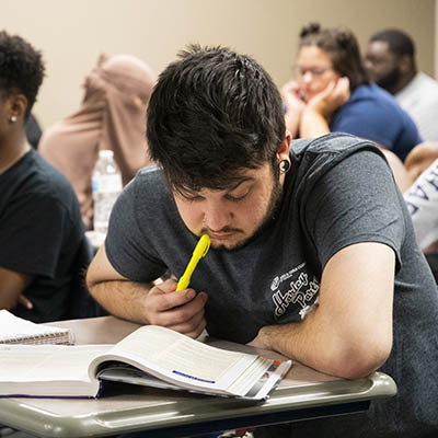 A student studies a book with a highlighter in hand.