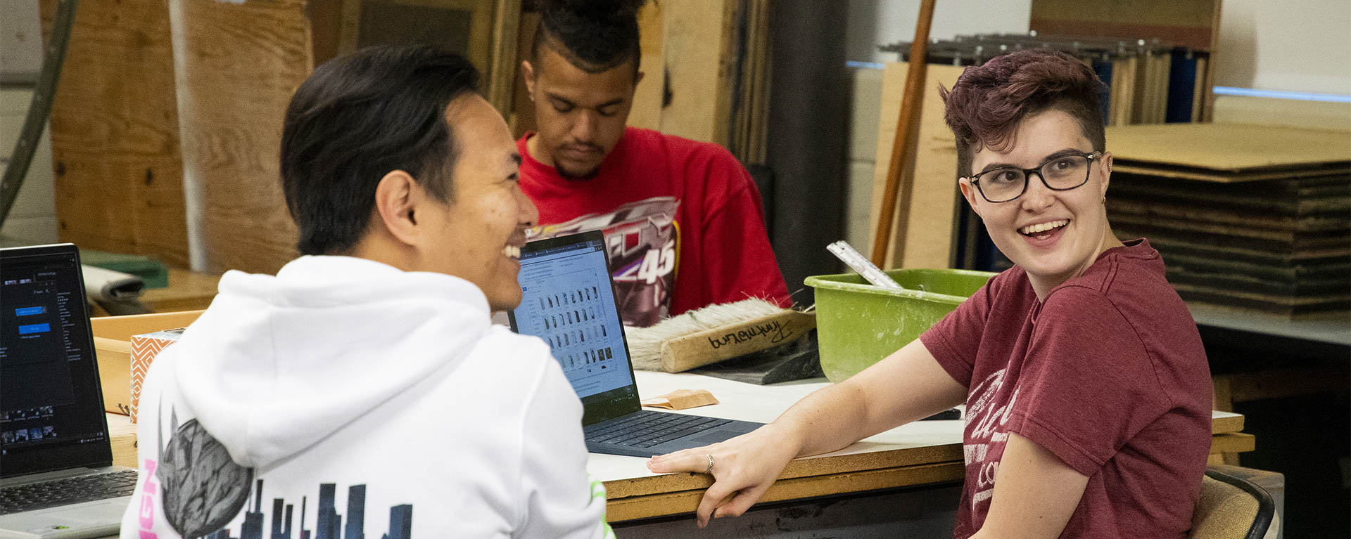 Art students smile while working at a table together.