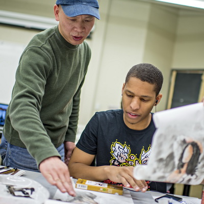 A professor gestures while helping a student that is sketching with pencil.