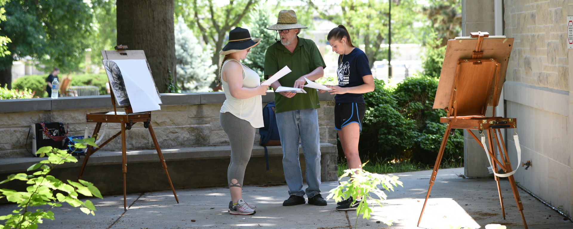 Students talking with professor outside while drawing with easels