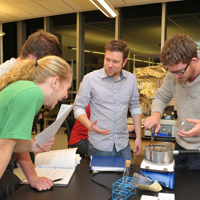 Chemistry students laugh while standing around a table with an experiment.