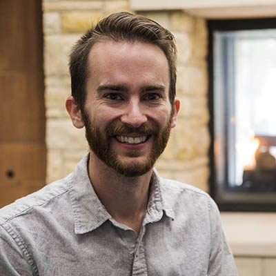 Brian smiles in front of a fireplace in Morgan Hall.