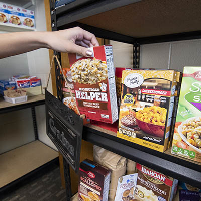 A hand pulls a box of hamburger helper off the shelf.