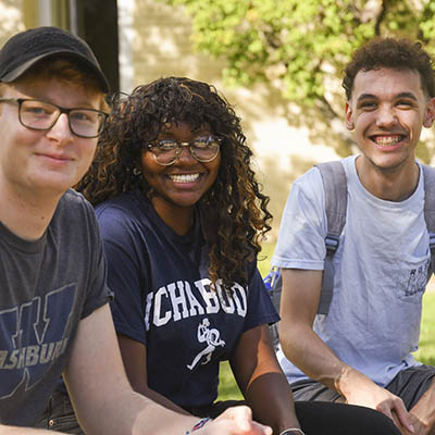 three students sitting outside smiling at camera