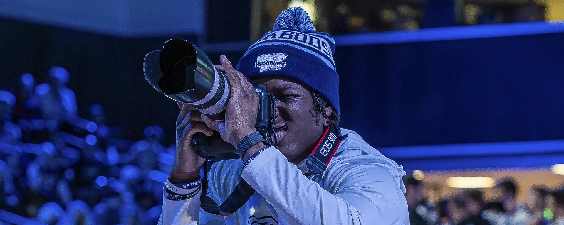 Student smiling while working a professional video camera at a basketball game
