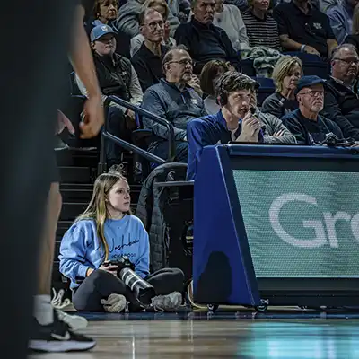 A student on the sideline at a basketball game with a professional camera