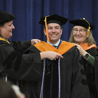 faculty put regalia on student graduation on stage