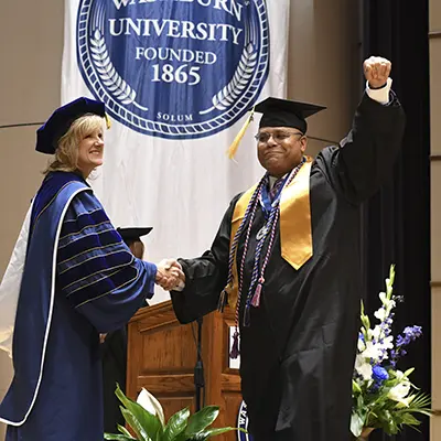 A graduate raises a fist in celebration while shaking hands with the president.