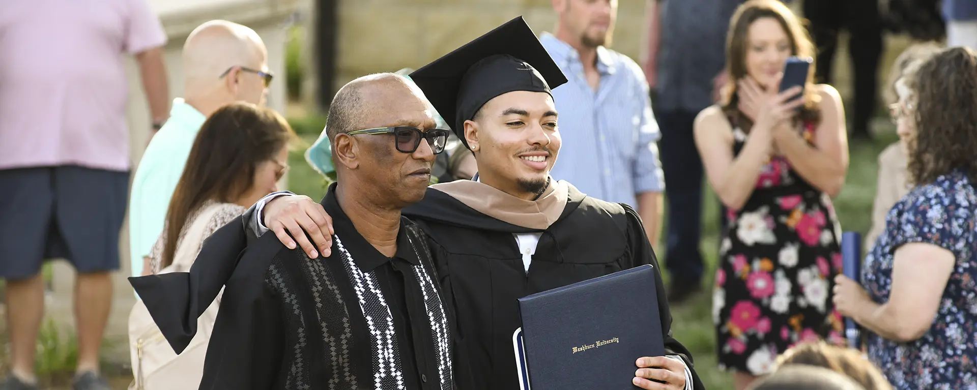 A graduate smiles with his family and diploma.