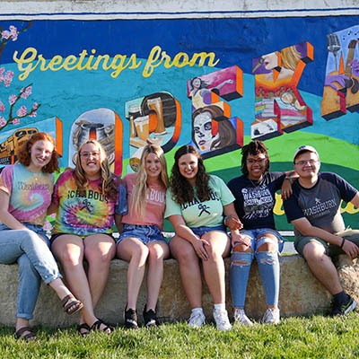 students in noto Topeka sitting in front of colorful mural