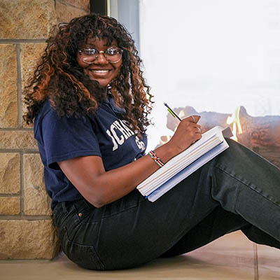 A student smiles while studying in front of a fireplace.