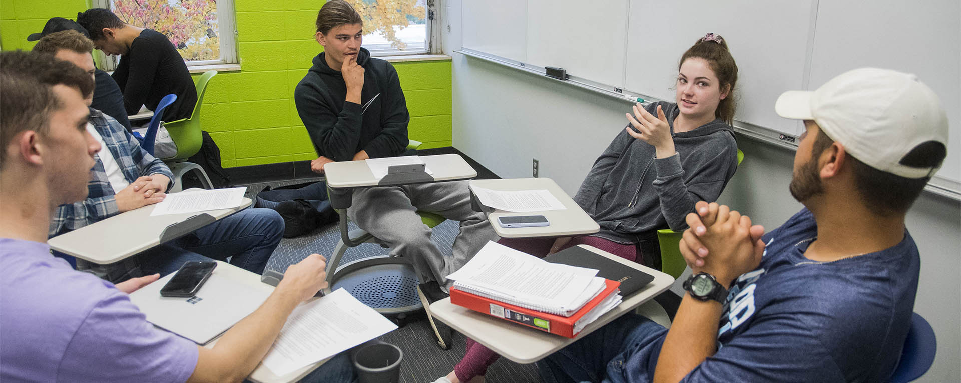 Students have a group discussion while sitting at desks arranged in a circle.