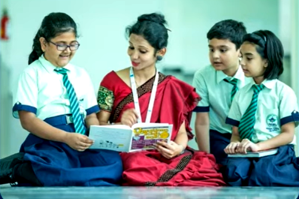 faculty member in red dress seated on floor with young students in another country