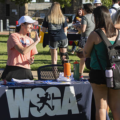 A student greets other students at a WSGA table at an event.