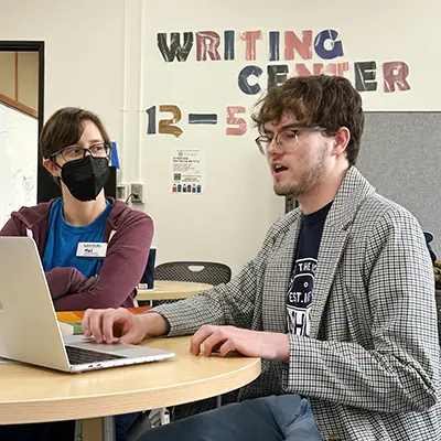 Two students smile while studying together with a laptop.