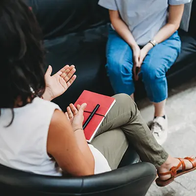 A counselor gestures while talking to a student while holding a notebook.