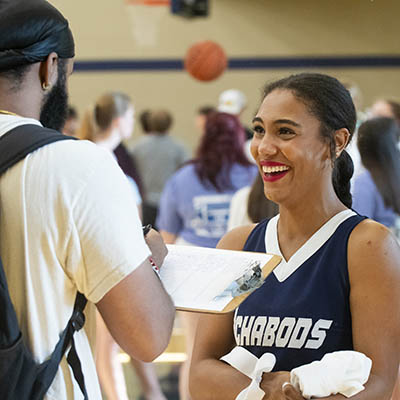 A cheer team member smiles while asking a student to sign up for something.